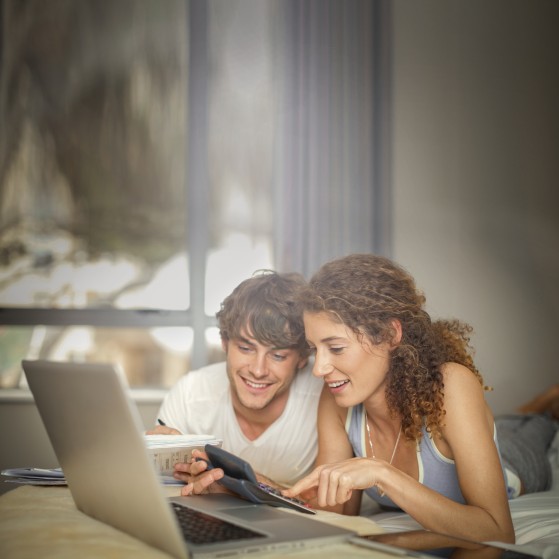 Junges Paar sitzt gemeinsam vor einem geöffneten Laptop