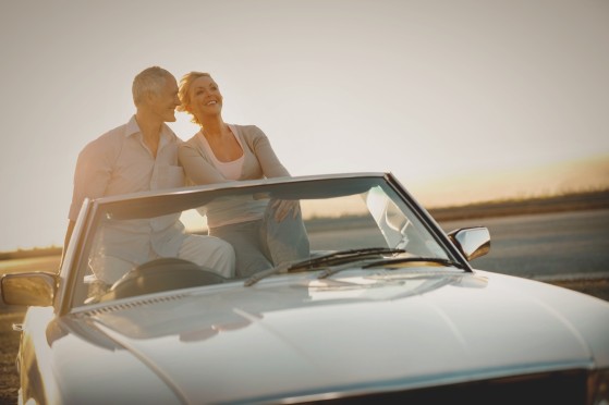 Paar steht im Gegenlicht in einem Cabrio, im Hintergrund Sonnenuntergang